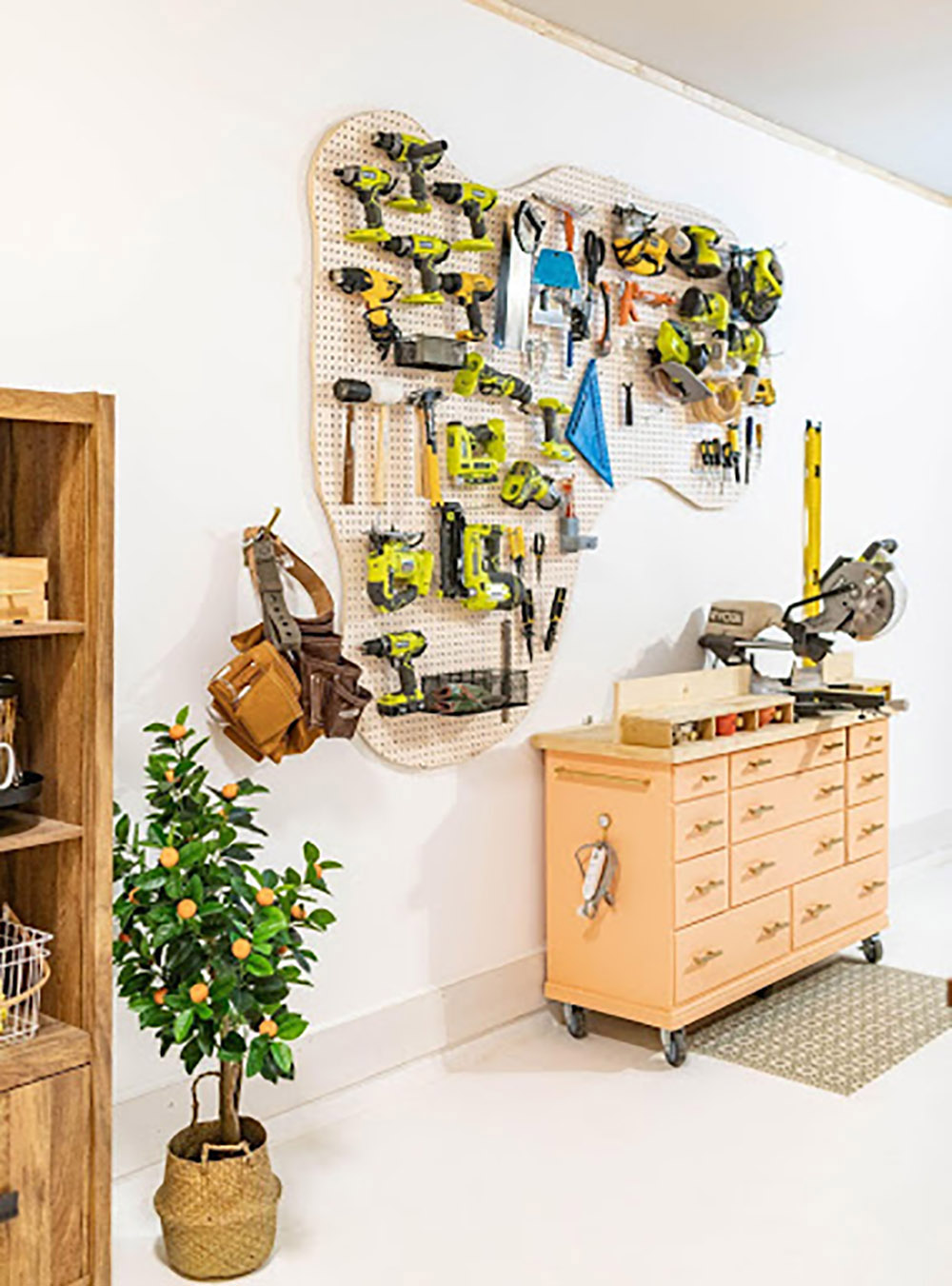 A wall of tools hanging on a pegboard hangs over a workbench with a saw.