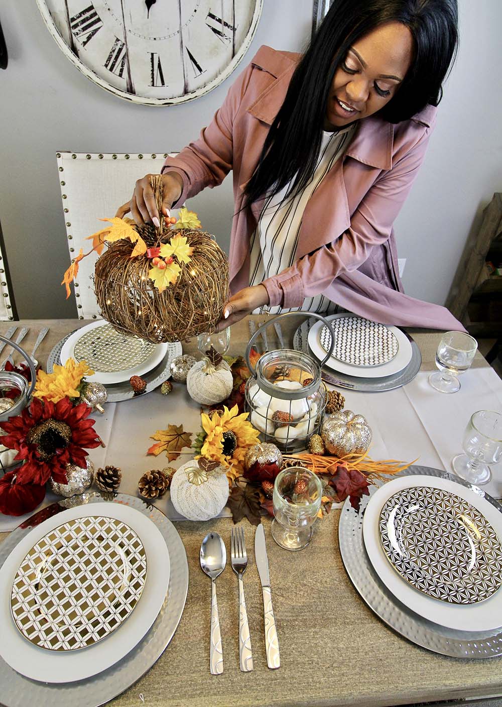 A woman adds a harvest twig pumpkin to the center of a table.