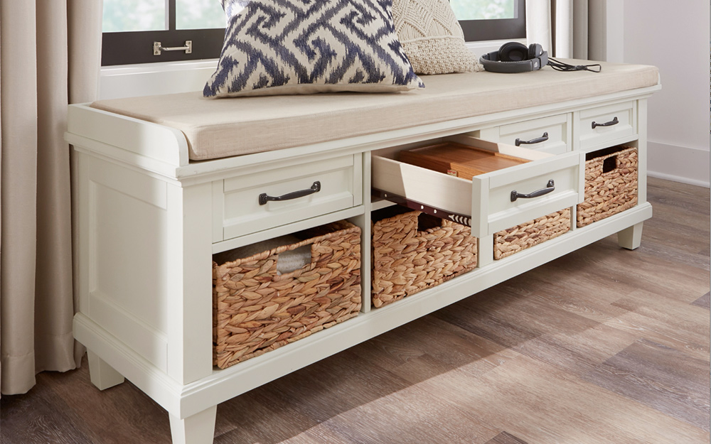 Two pillows sit on top of a bench seat with drawers and baskets used for storage.