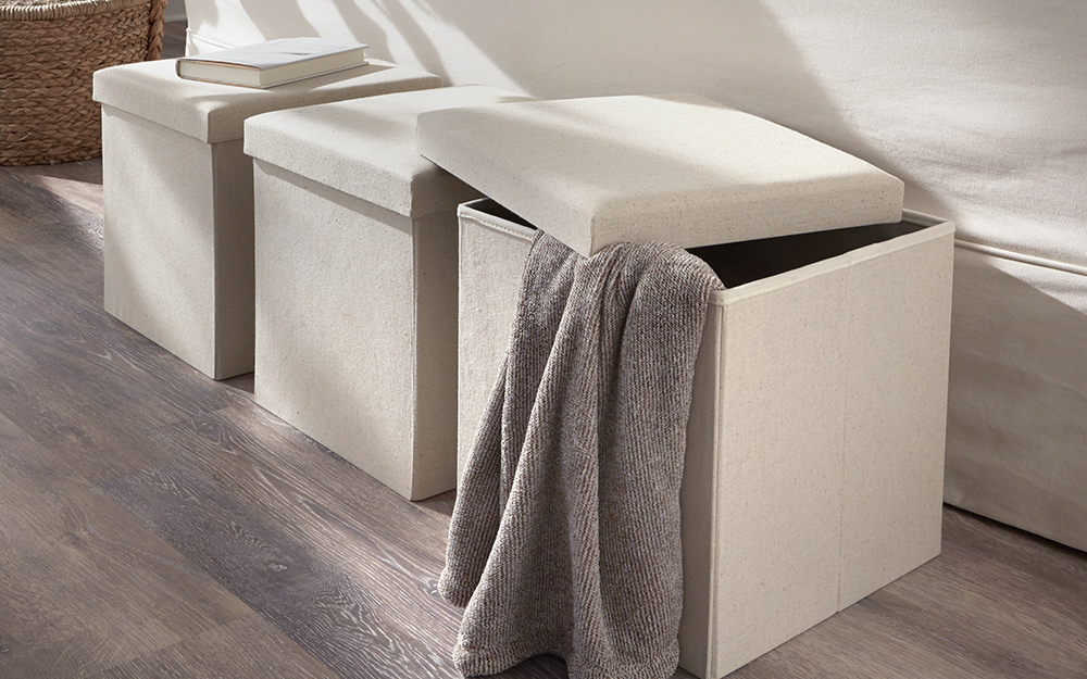 A gray blanket hangs out of the open lid of a storage ottoman. 