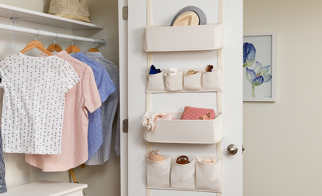 A hat, a scarf and a purse are stored in canvas pouches in an over-the-door storage unit. 