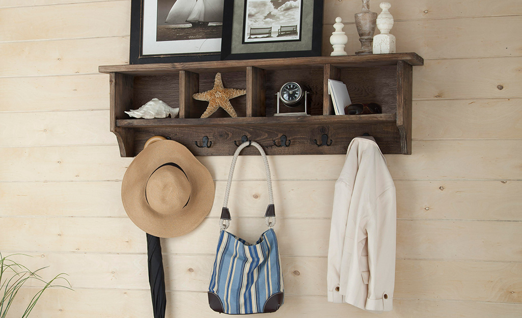 A hat, a tote bag and a jacket hang on a hooks under a rustic wooden shelf.
