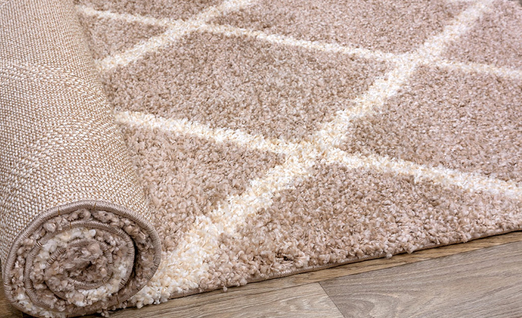 A rug is partially unrolled over a wood floor.