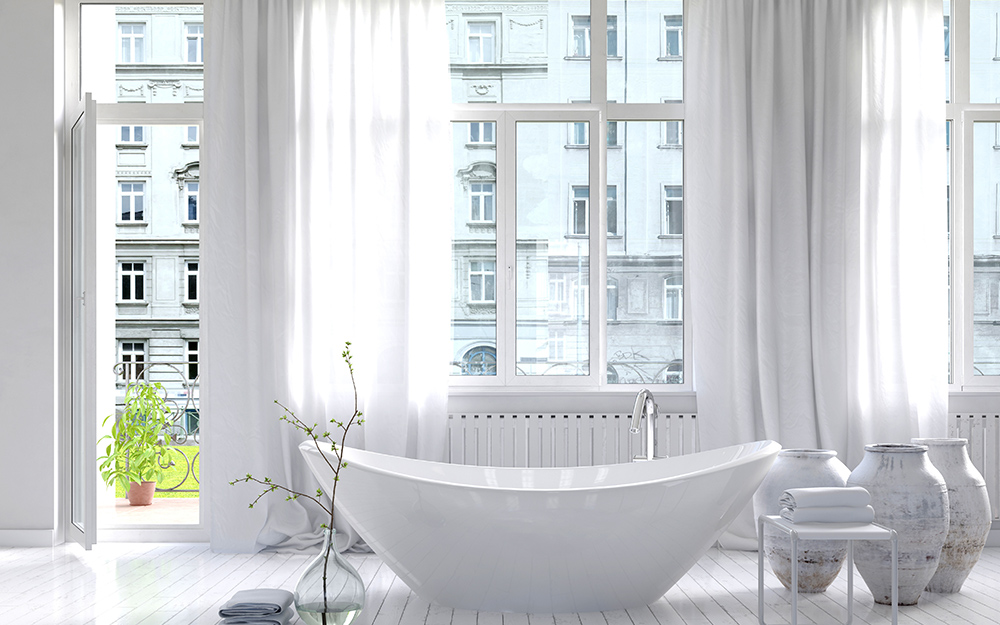 A bathroom with white curtains hanging over the windows.