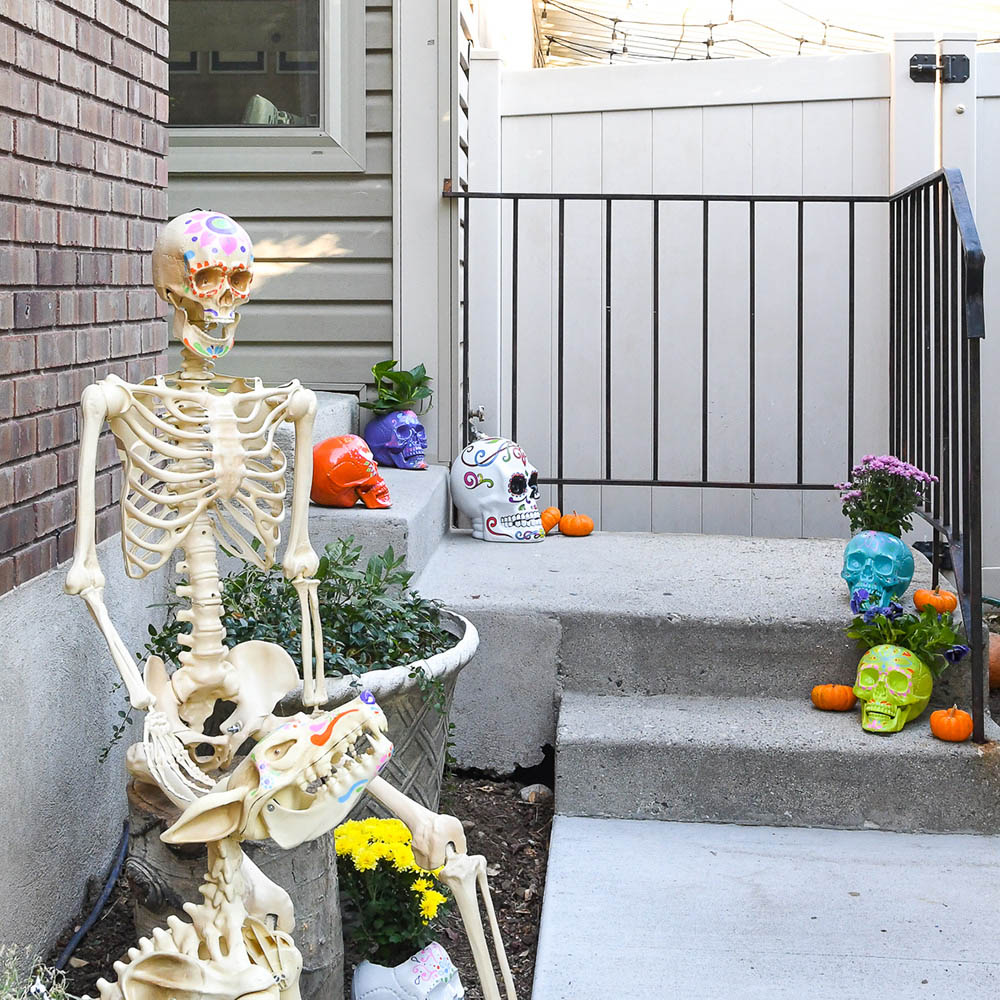 A front porch decorated with a skeleton and brightly colored skeleton heads.