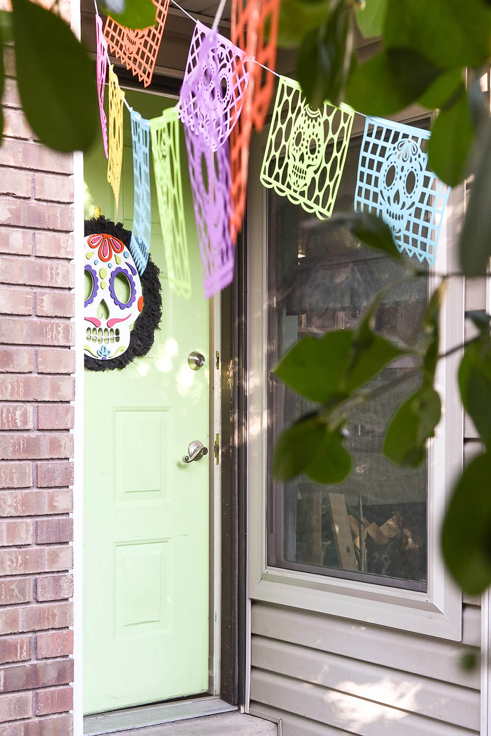 A Day of the Dead banner hanging in front of a green door with a sugar skull wreath.