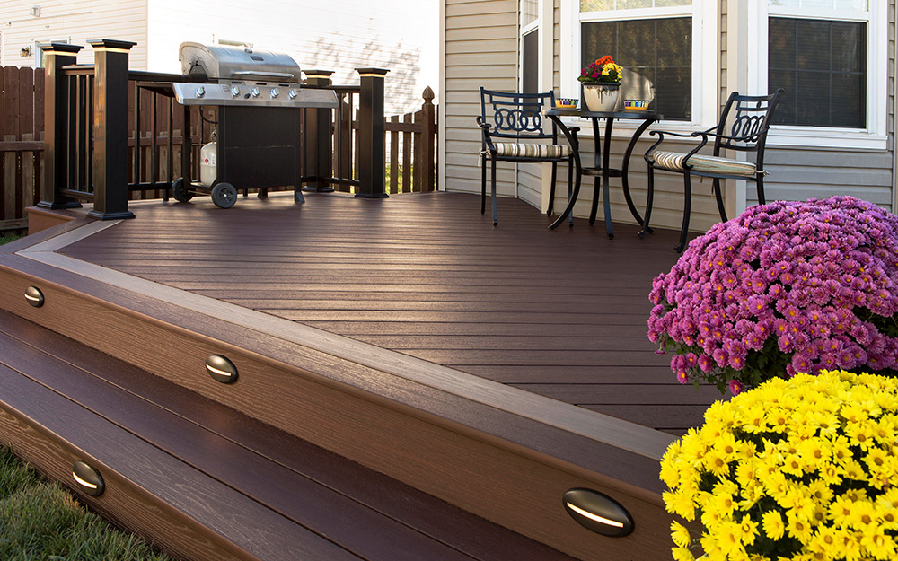 A grill, furniture and potted flowers sit on a deck with boards made of mountain redwood.