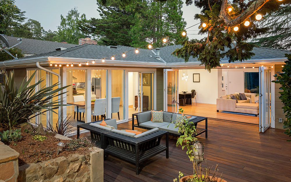 String lights hang over an attached platform deck with patio furniture and wide doors leading into a living room.