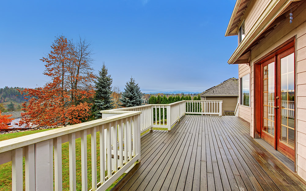Double doors lead out to a wraparound wooden deck with a white railing.