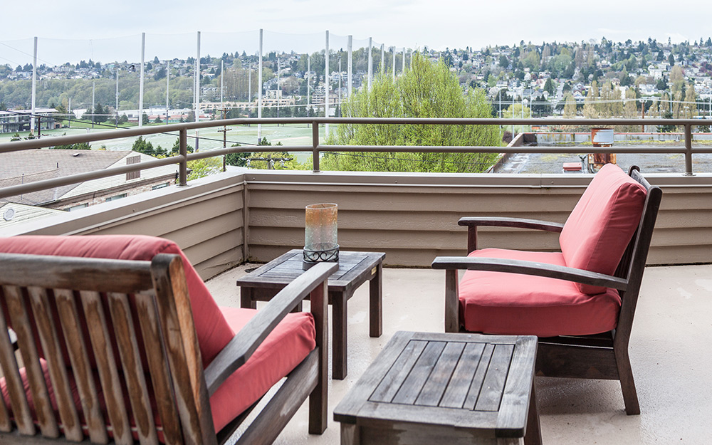 Red armchairs sit on a rooftop deck that affords a view of the neighborhood.