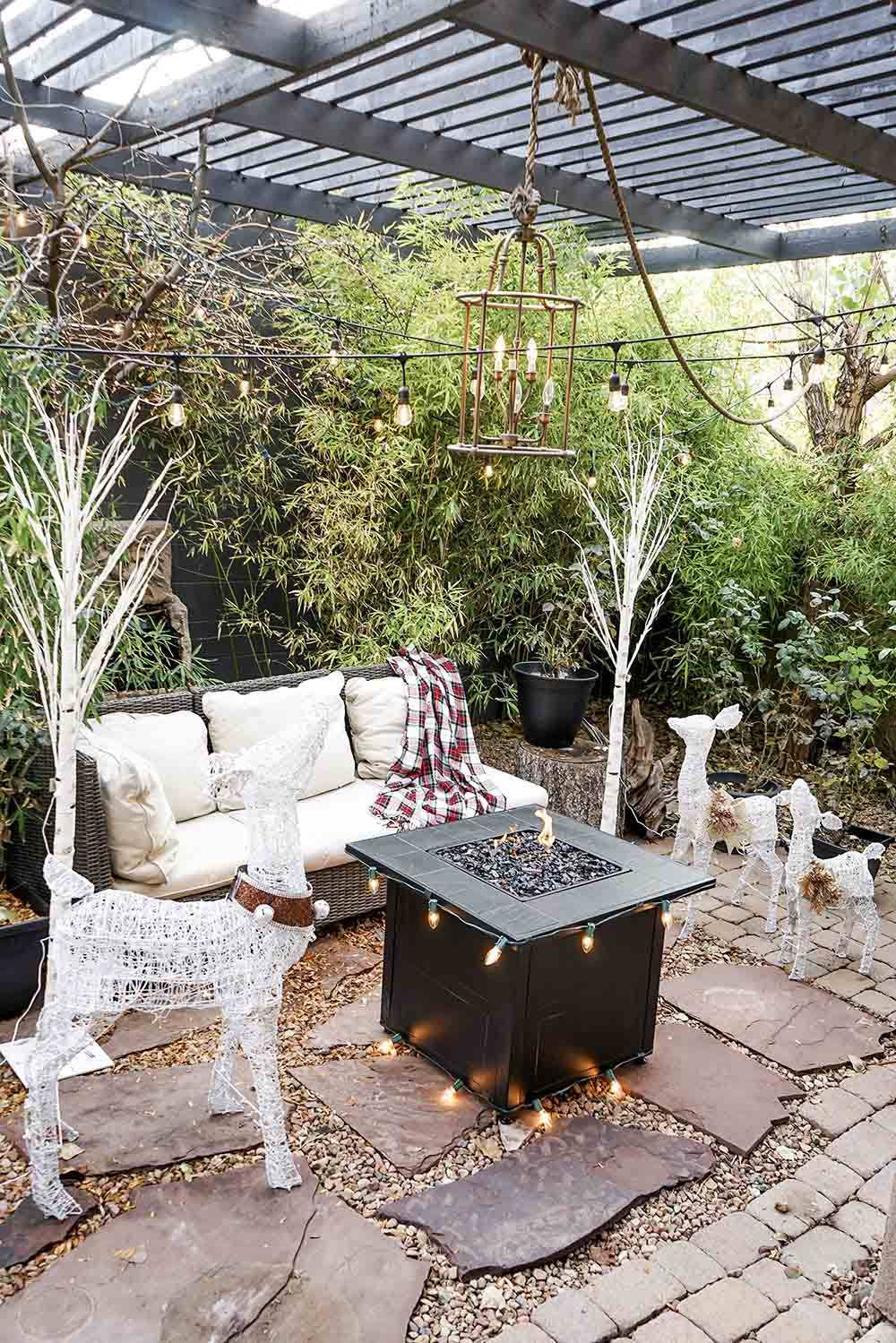 An outdoor patio with string lights, LED white lighted deer, and a fire pit.