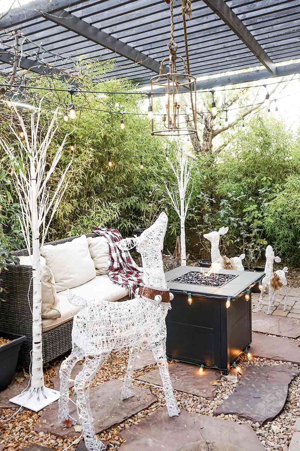 A patio decorated for the holidays with white LED birch trees and deer.