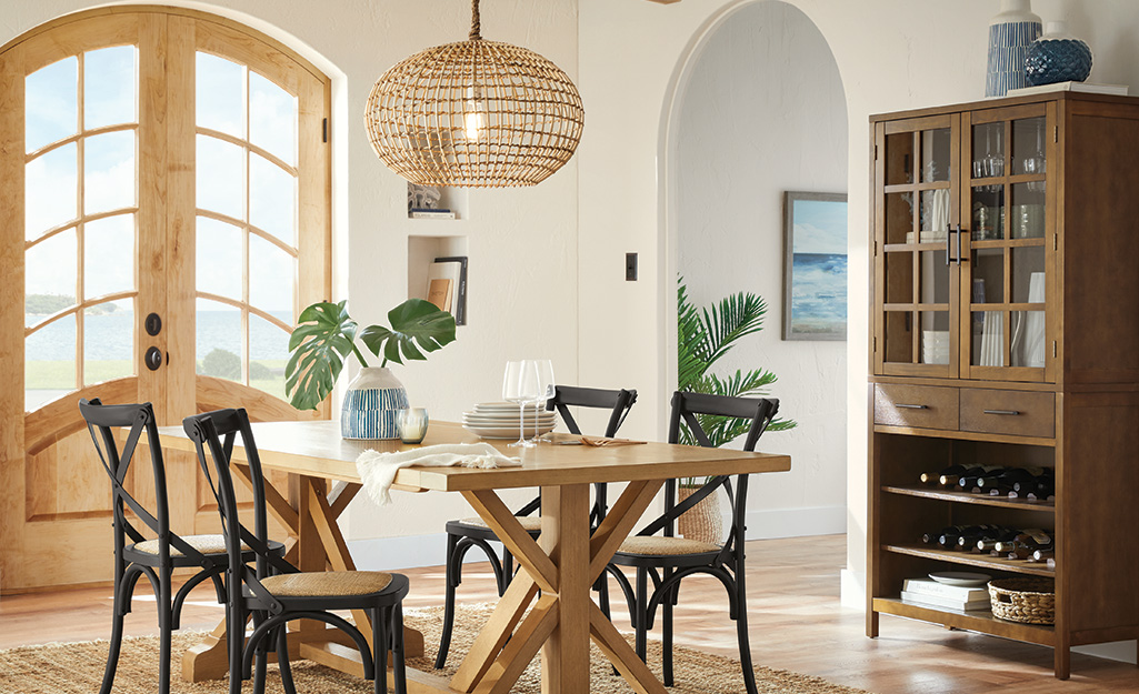 A wicker pendant light suspended over a dark and light wood dining set.