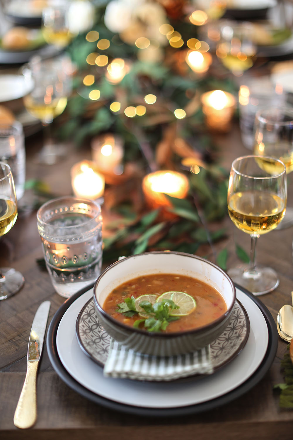 A table decorated with candles and a place setting with a full bowl of soup. A table decorated with candles and a place setting with a full bowl of soup.