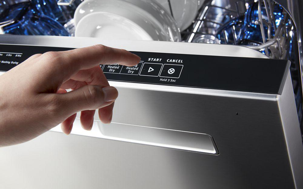 A hand reaching to press start on the top control panel of a dishwasher.