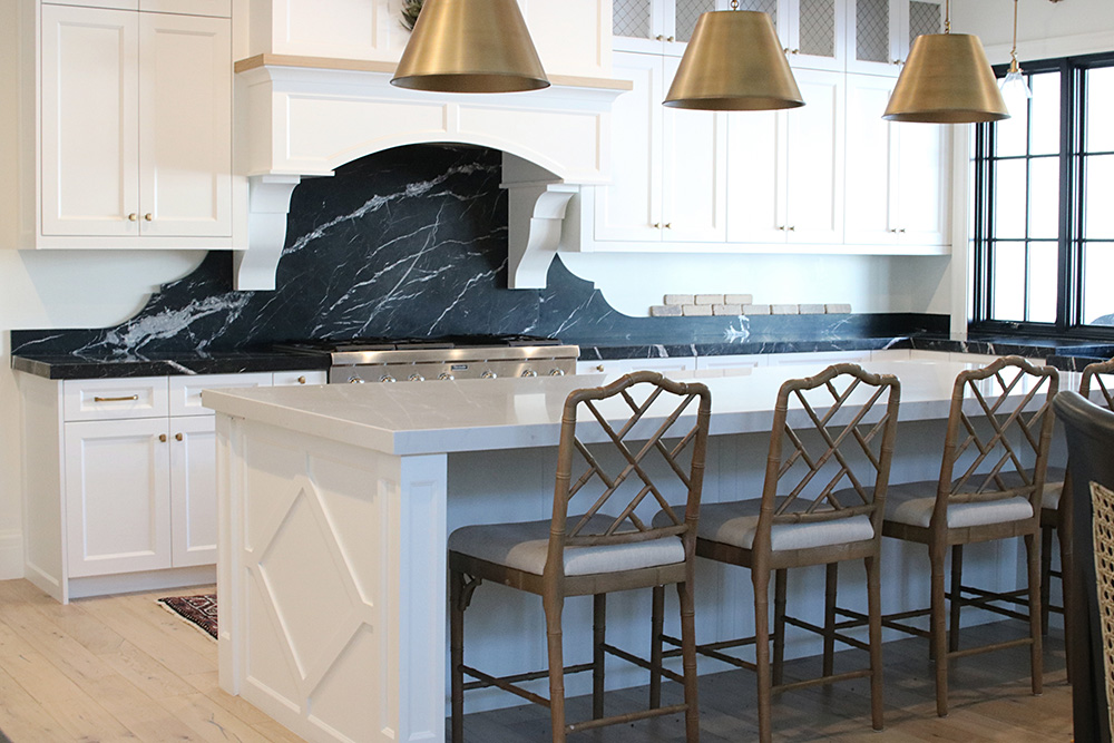 A kitchen with white cabinets and a black marble backsplash.