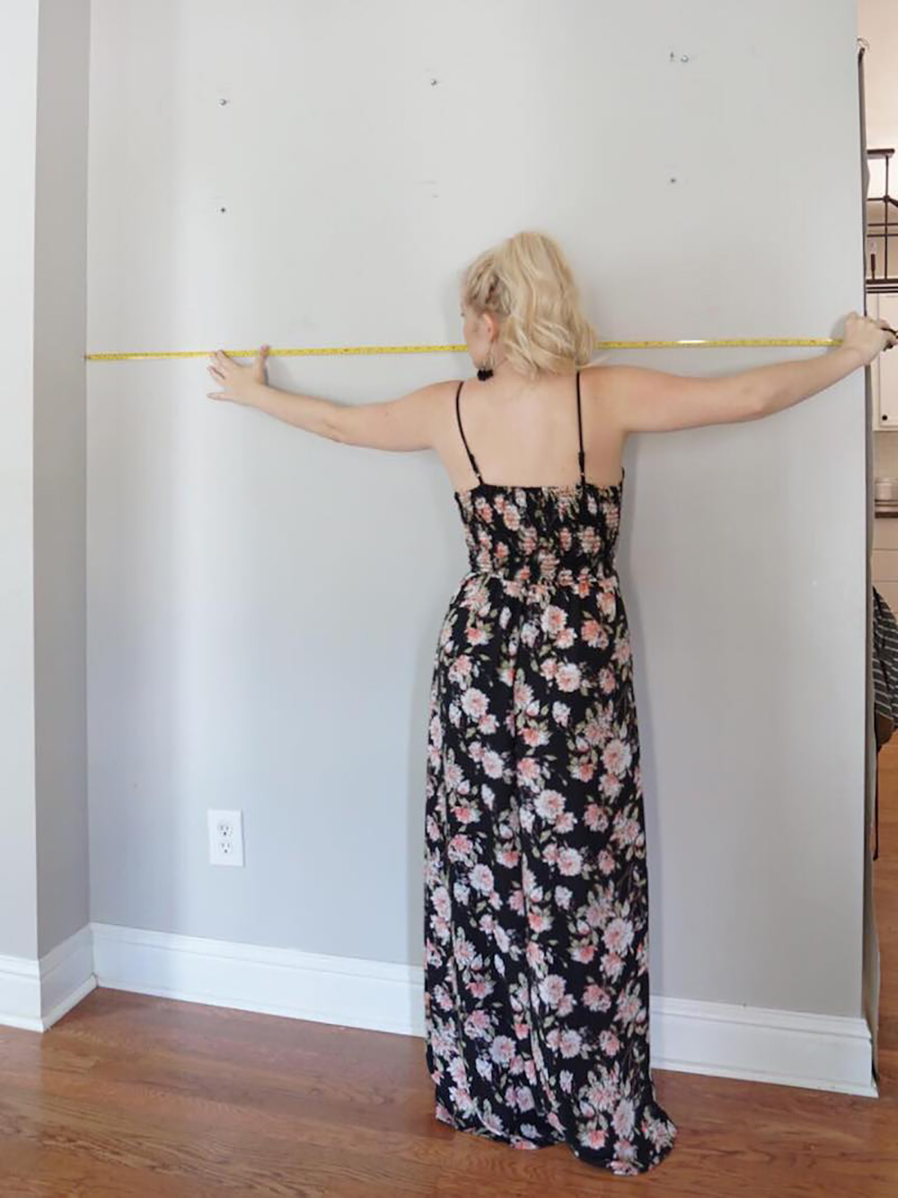 A woman measures a wall with a tape measurer.