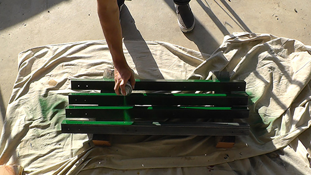 A person painting the angle irons with green spray paint.