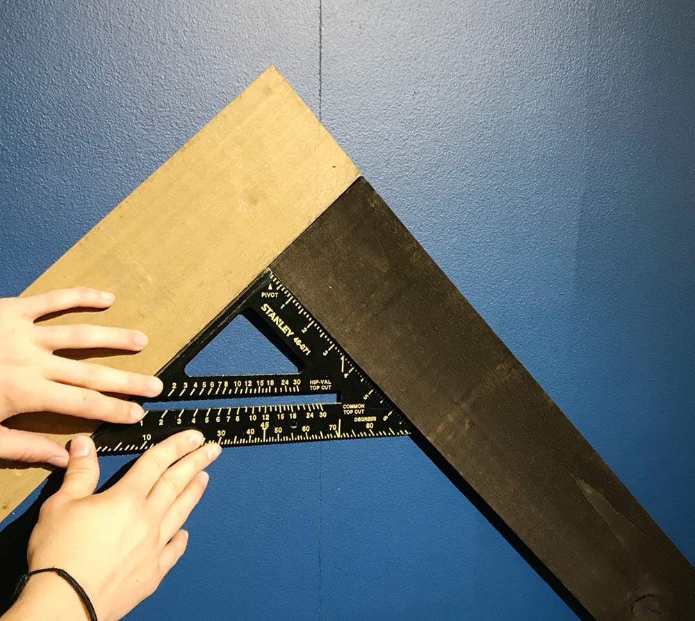 A person uses a speed square to line up two weathered wood boards. A person uses a speed square to line up two weathered wood boards.