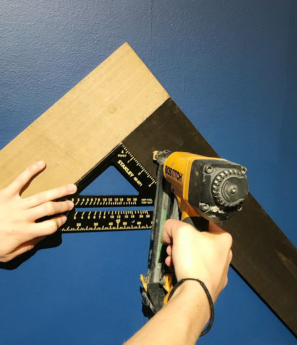 A person attaches a weathered wood board to a wall with a nail gun. A person attaches a weathered wood board to a wall with a nail gun.