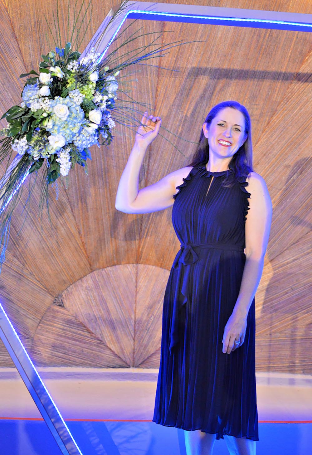 A woman wearing a dark colored dress stands next to flowers hanging on a DIY hexagon backdrop.