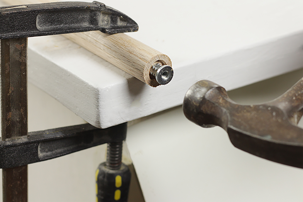 A hammer drives an insert nut into the end of a securely clamped dowel.