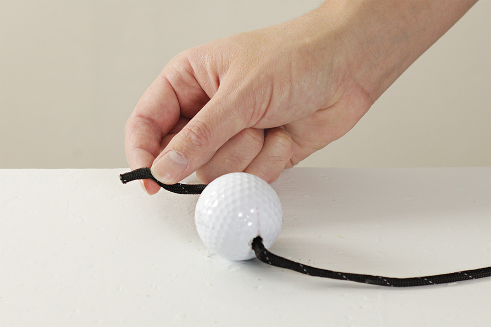 A person threading black rope into the hole in a golf ball to create one of the bolos.