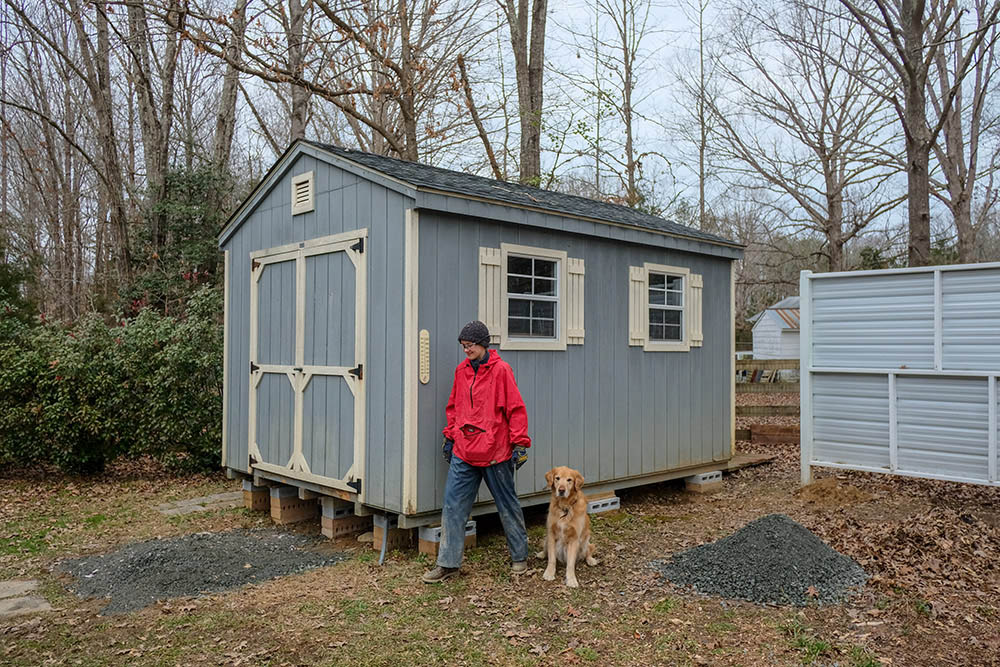 A person and a dog standing in front of a shed.