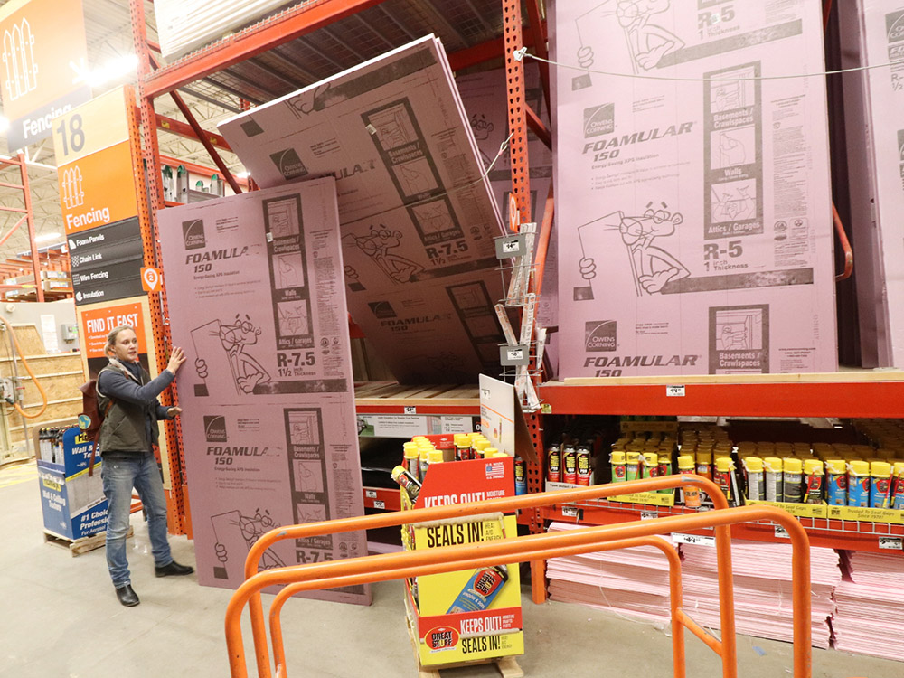 A person holding a pink sheet of insulation inside a Home Depot store.