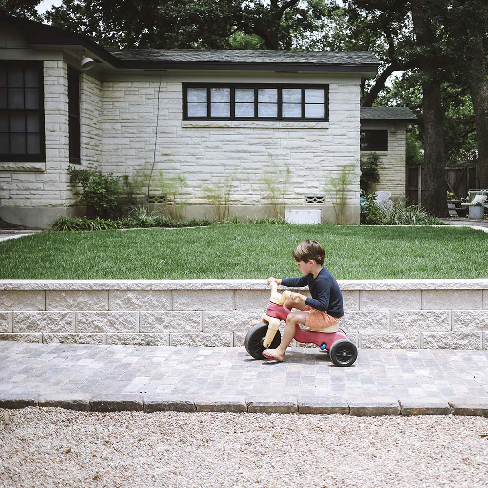 A young boy riding a tricycle in front of a home.