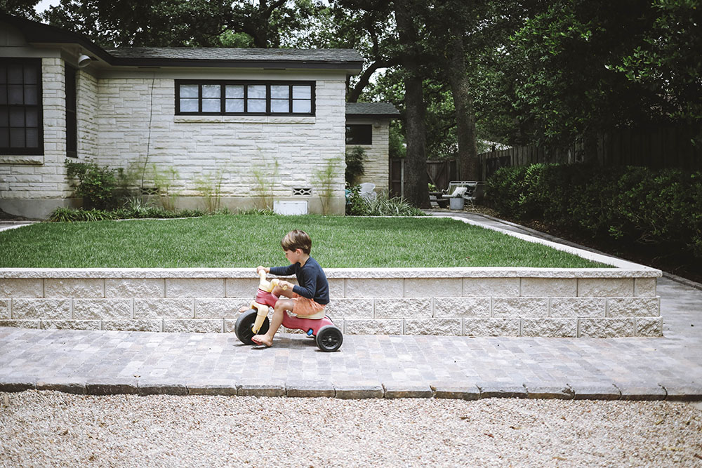 A young boy riding a tricycle on a paver path.