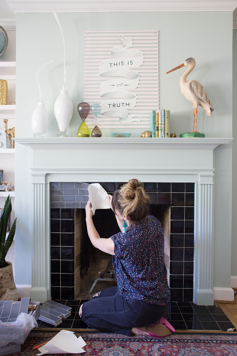 A woman sticking gray Smart Tiles over black tile on a fireplace.