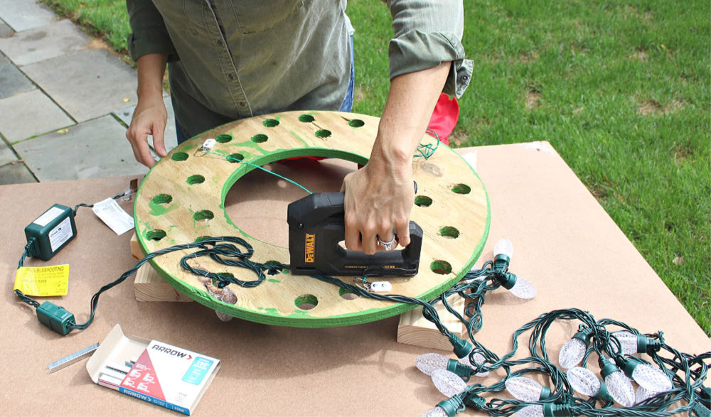 A person attaches light bulbs to a wooden wreath cut out of plywood.