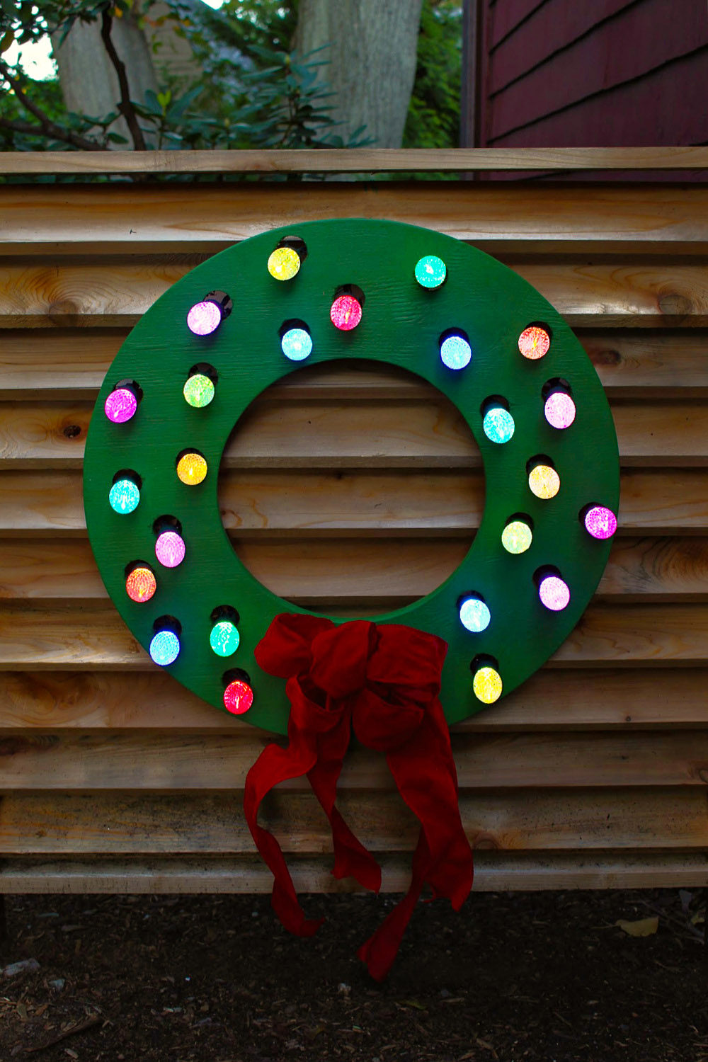 A completed DIY wood wreath cut out with Christmas lights and a bow.