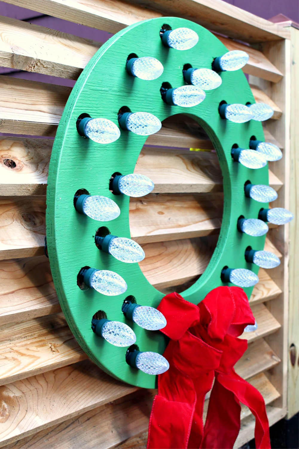 A green wooden wreath with lights and a red bow.