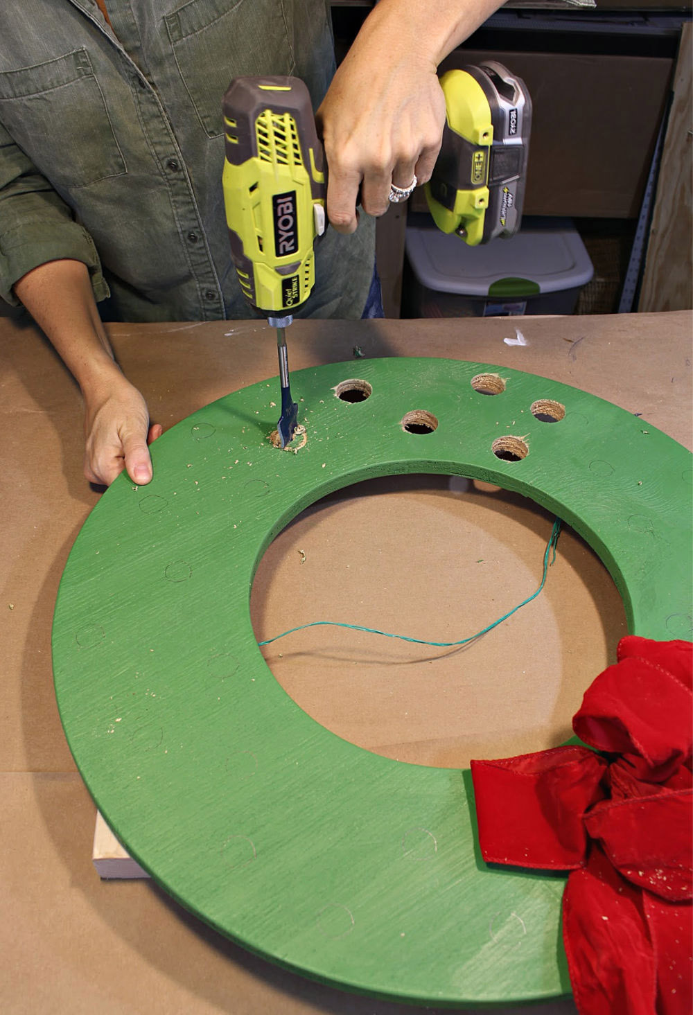 A person drills holes in a green wood wreath cut out.