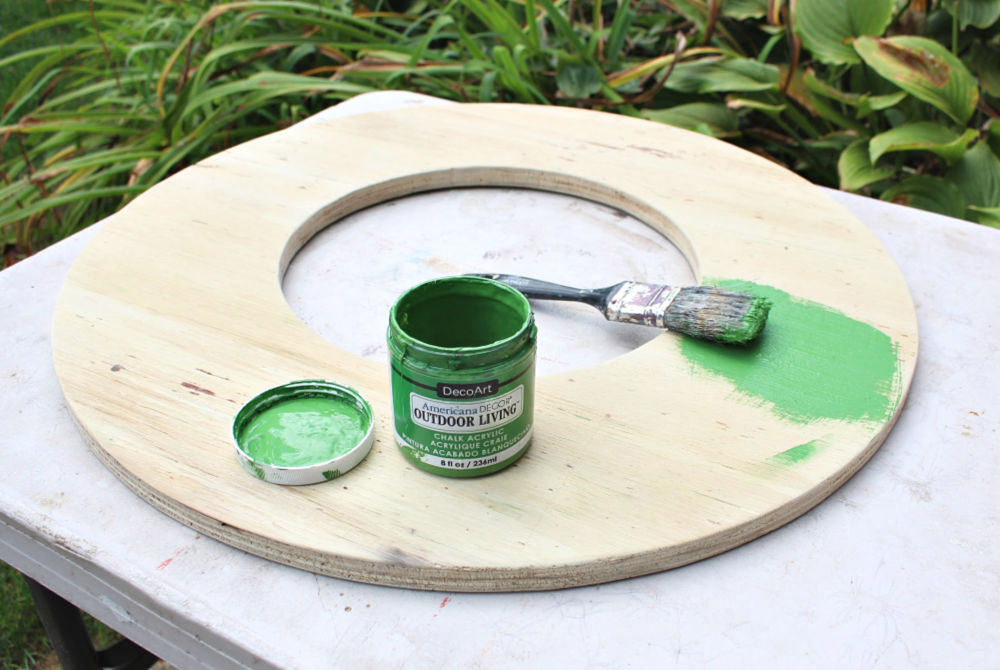 A paintbrush and green paint sitting on a wooden wreath cut out.
