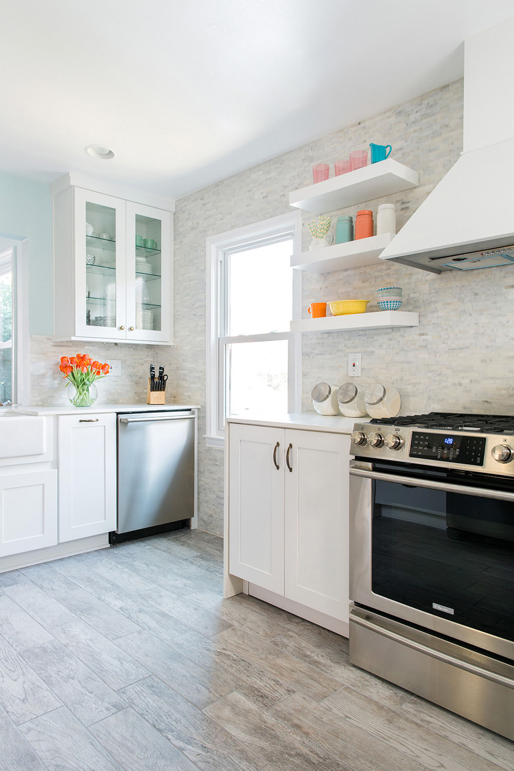 Remodeled kitchen with vinyl flooring, white cabinets, an oven with a white vent hood, and white shelving.