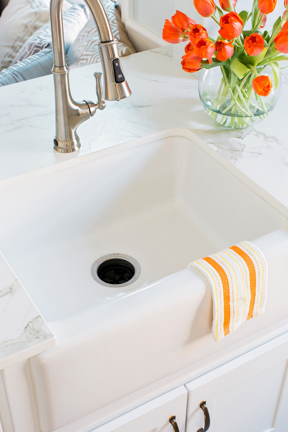 White sink with a silver faucet, a dish towel and fresh flowers on the countertop. 