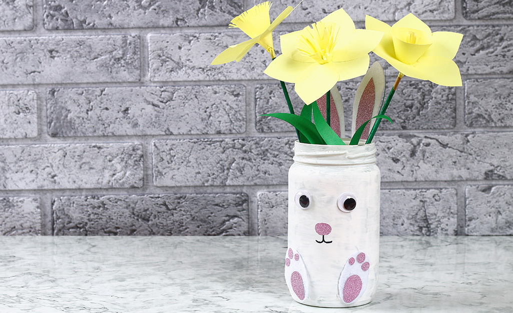 A Mason jar made to look like a white bunny holds flowers.