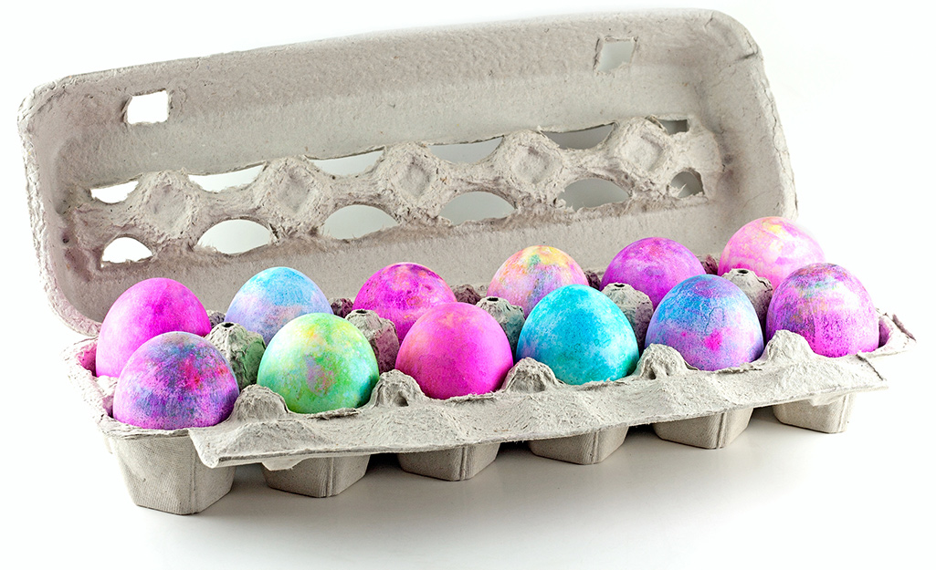 Easter eggs dyed with shaving cream and neon dye sit in an egg carton.