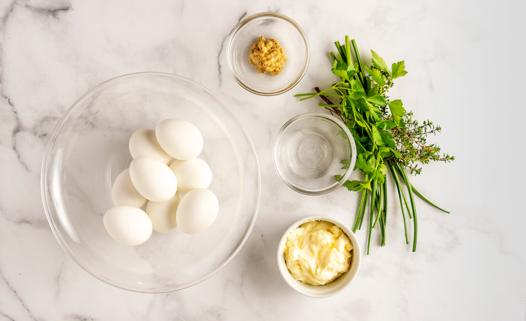 A bowl of white eggs, mustard, mayo and fresh herbs on a table. A bowl of white eggs, mustard, mayo and fresh herbs on a table.