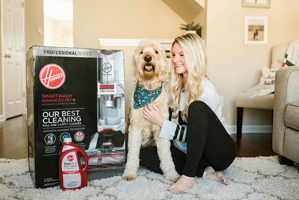 A woman and a dog sitting on a rug next to a Hoover SmartWash advanced pet carpet cleaner box.