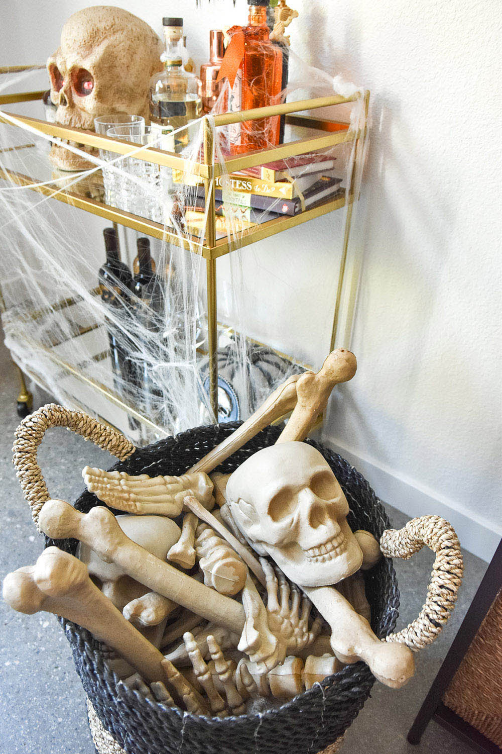 A basket filled with skeleton bones sits next to a bar cart decorated with spider webs.