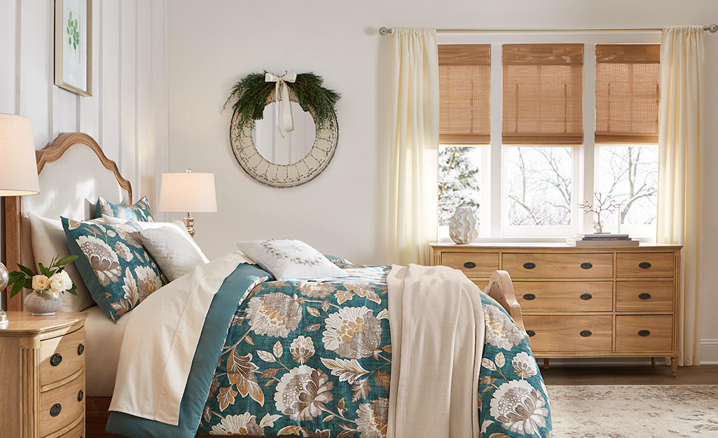 A bedroom with wood blinds and sheer drapes on the window.