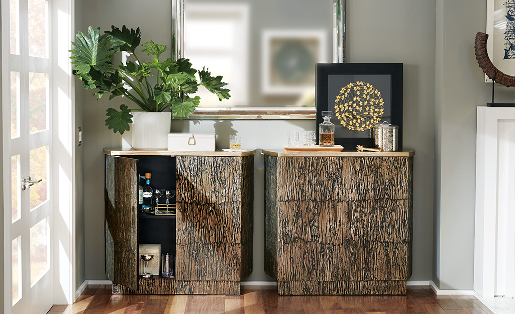 Carved brown storage cabinet topped with art and greenery.