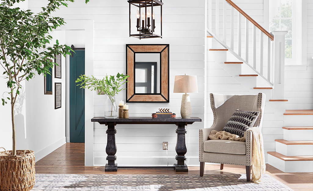 A black console table and upholstered chair in an entryway.