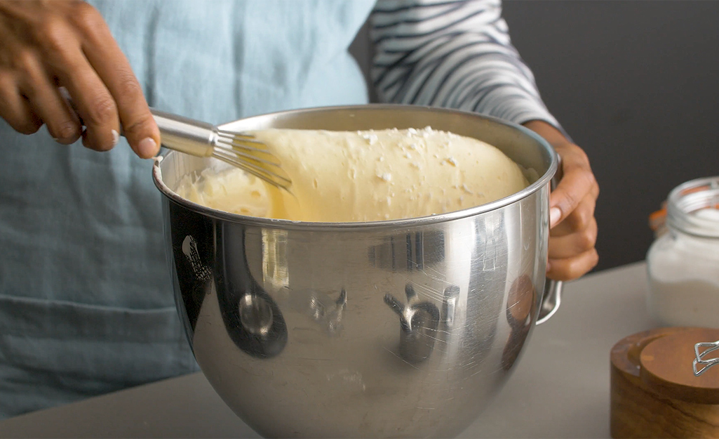 Someone whisking cake batter in a large silver mixing bowl