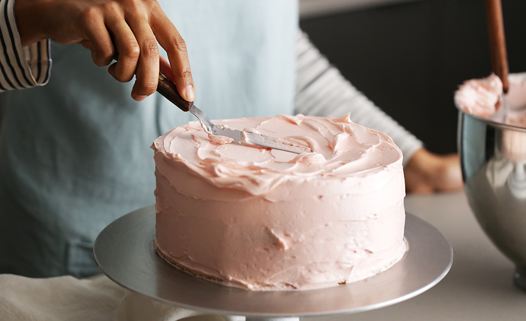 Someone using a spatula to put pink icing on a cake
