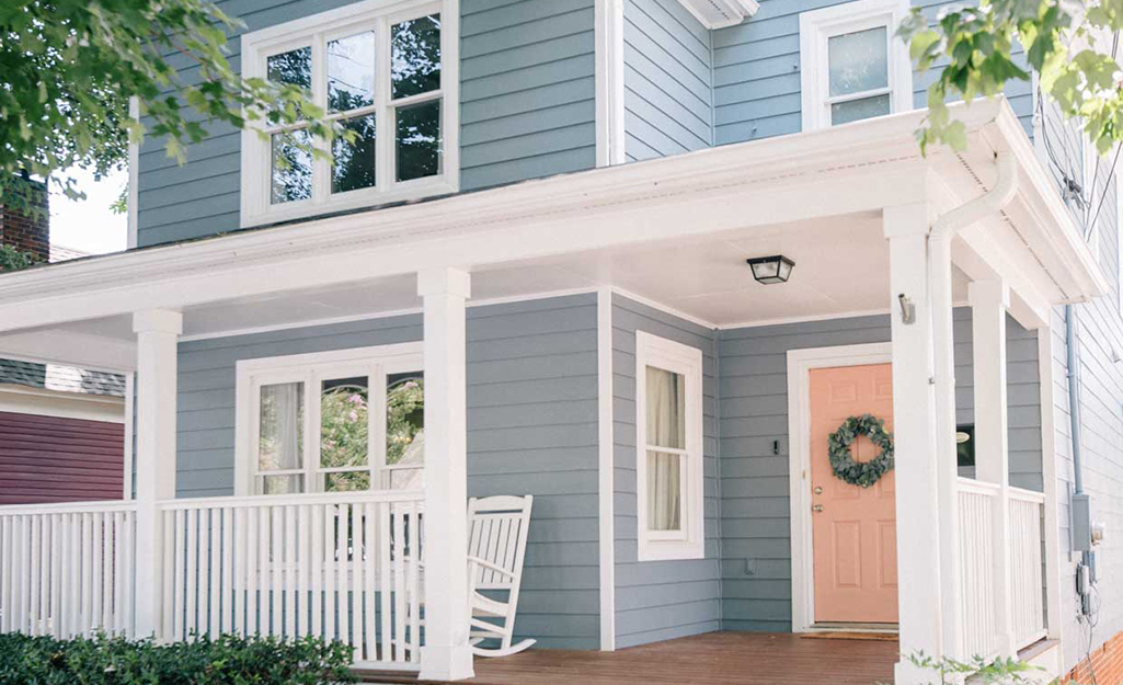 The blue-gray exterior of a two-story home pairs well with white trim along the front porch rails and a coral front door.